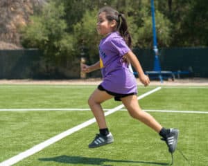young girl leaping across a field at Camp Erin