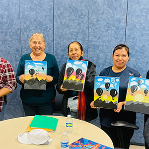 Group of women holding paintings they did as part of the Spanish Community Program